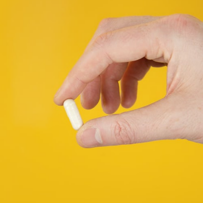 Hand holding white capsule on yellow background
